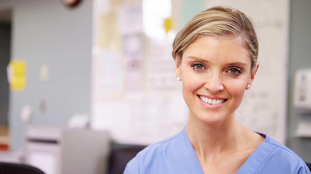 a frame physician with her hair up and in blue scrubs is smiling