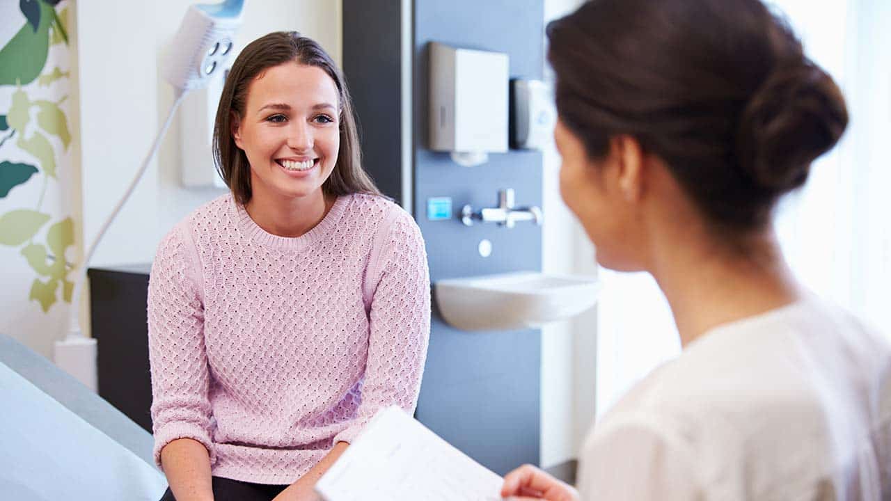 a new client discusses prescription medication at the clinic the client is sitting on an emanation table facing the doctor
